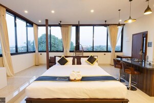 A hotel room with a large bed, a minibar, a seating area, and large windows offering a view.
