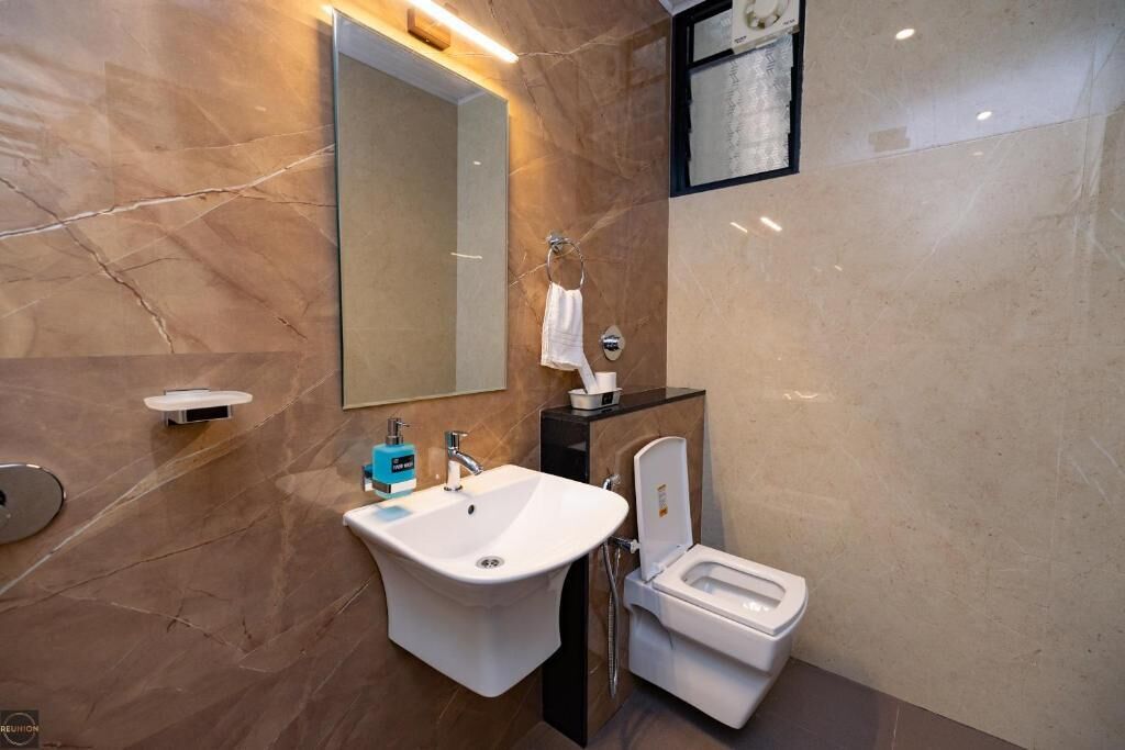 A modern bathroom with a marble wall, a white sink, a toilet, and a mirror.