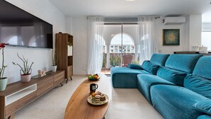 Uma sala de estar moderna com um sofá, uma mesa de centro com doces, uma televisão e uma varanda com vista.