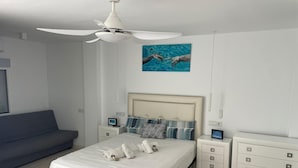 Um quarto moderno com cama, mesas de cabeceira, um banco, um ventilador de teto e uma pintura.