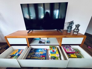Ein Fernseher auf einem Holzständer mit zwei Schubladen darunter, die Brettspiele enthalten.