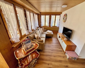 Ein gemütliches Wohnzimmer mit einer Couch, einem Fernseher und einem kleinen Wagen mit Zeitschriften.