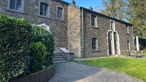Un bâtiment en pierre avec une entrée pavée, un petit escalier et une pelouse.