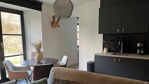 Une cuisine moderne avec des meubles de couleur sombre, une machine à café et un évier. On y trouve également un coin repas avec une table ronde et des chaises.