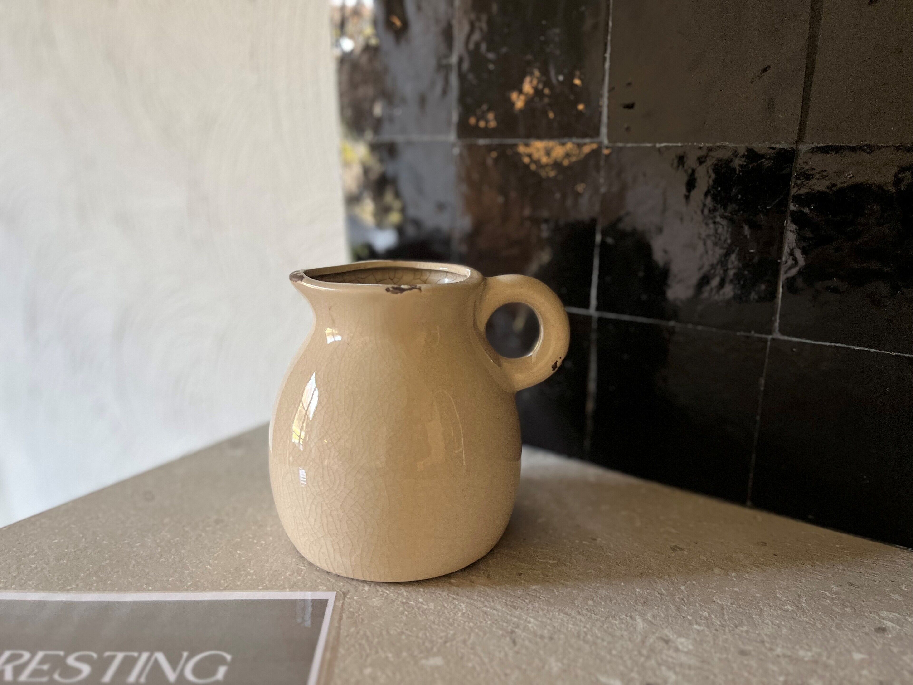 Un pichet en céramique beige est posé sur un comptoir, et un panneau indiquant « EN PAUSE » se trouve au premier plan.
