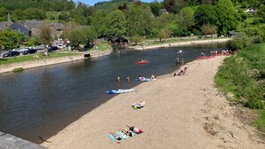 Une plage au bord de la rivière où l’on peut faire du kayak, une rive sablonneuse et, en arrière-plan, une colline boisée.