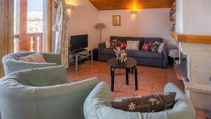 A living room with a sofa, armchairs, a coffee table, a television, and a fireplace. - Retreat With Panoramic Alpine Views (Landry)