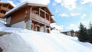 A wooden chalet with a balcony, stone foundation, and snow-covered surroundings. - Retreat With Panoramic Alpine Views (Landry)