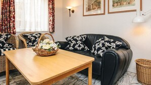 A living room with a black leather sofa, two wicker chairs, a wooden table, and a basket of flowers. - 4 Person Holiday Home in Brovst (Brovst)