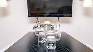 A flat-screen TV mounted on a wall, two wall-mounted lamps, and a table with three clear glass vases with flowers. - 4 Person Holiday Home in Brovst (Brovst)