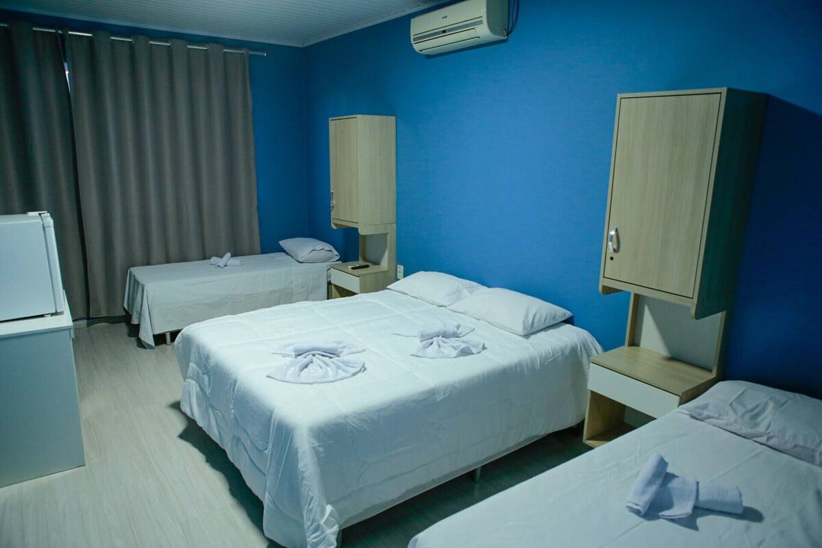 Habitación de hotel con dos camas, un escritorio, una silla, un armario y un equipo de aire acondicionado.
