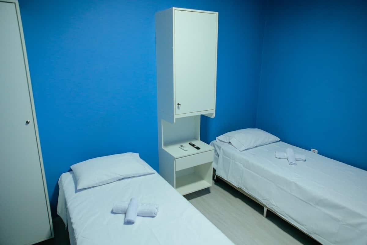 Una habitación con dos camas, un armario, una mesita de noche y un pequeño estante.