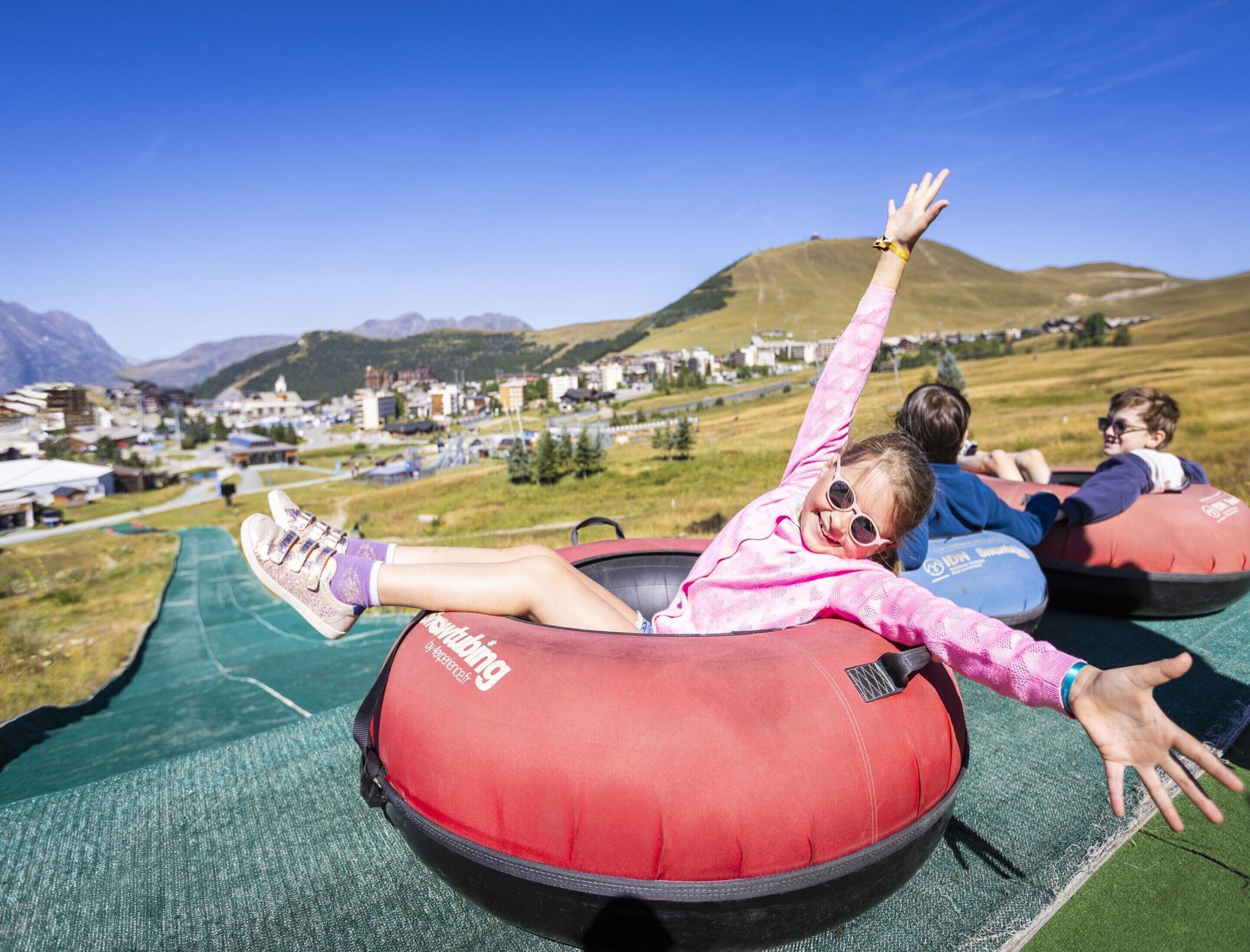 Des personnes sur une pente où l’on fait de la luge, avec une ville et des montagnes en arrière-plan.