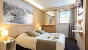 A hotel room with a bed, bedside lamps, a telephone, a painting of a snowy landscape, and a window with curtains. - Retreat With Shared Pool and Terrace (Huez)