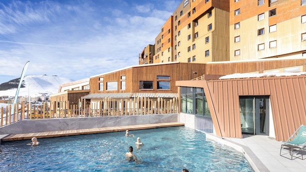 A swimming pool with a wooden deck and a modern building in the background. - Retreat With Shared Pool and Terrace (Huez)