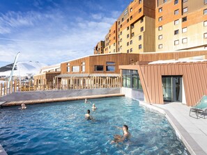 A swimming pool with a wooden deck and a modern building in the background. - Retreat With Shared Pool and Terrace (Huez)