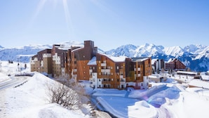 A modern building with multiple floors, a ski slope, and snow-covered mountains in the background. - Retreat With Shared Pool and Terrace (Huez)
