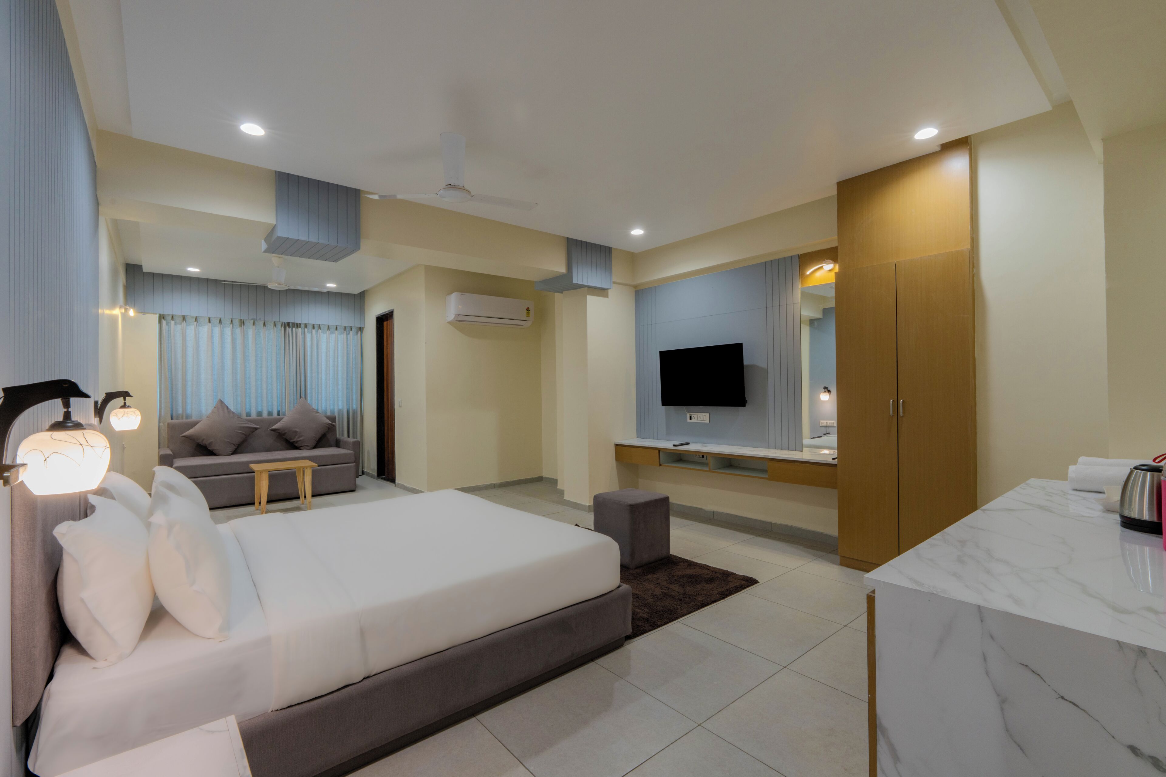 A modern hotel room with a bed, a sofa, a TV, a desk, and a bathroom.