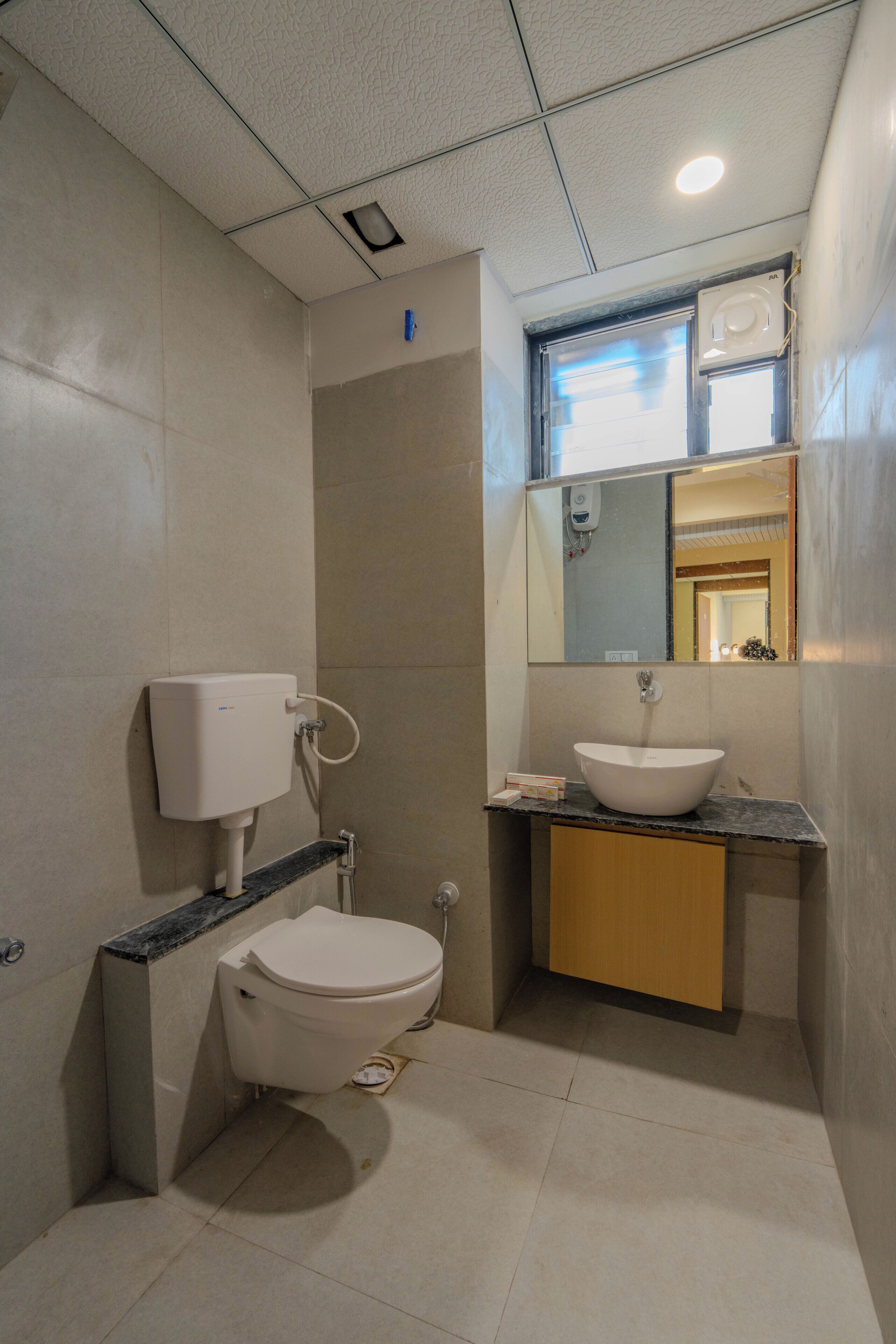 A bathroom with a toilet, sink, mirror, and a ceiling light.