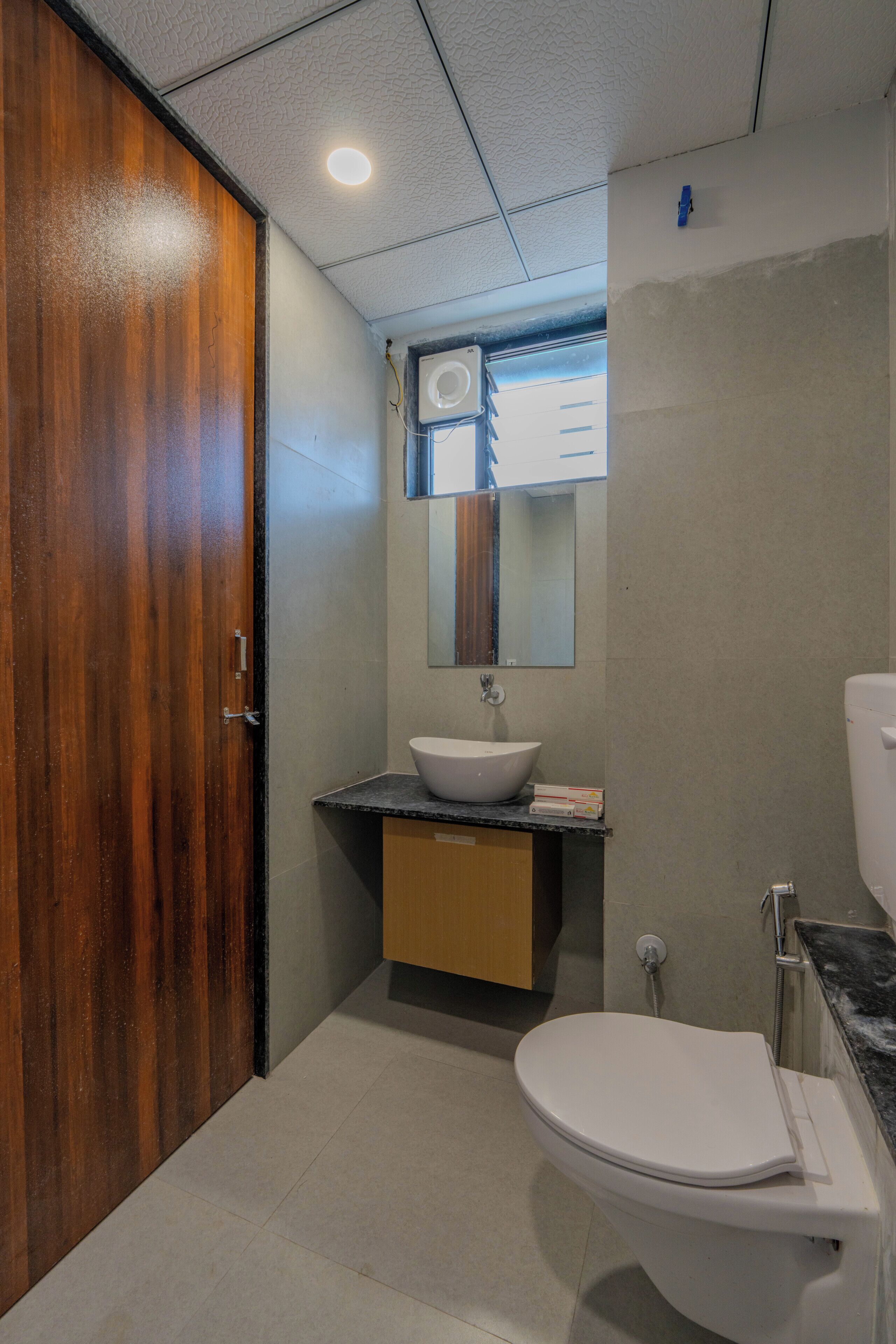Un baño con puerta de madera, lavamanos blanco, espejo y retrete.