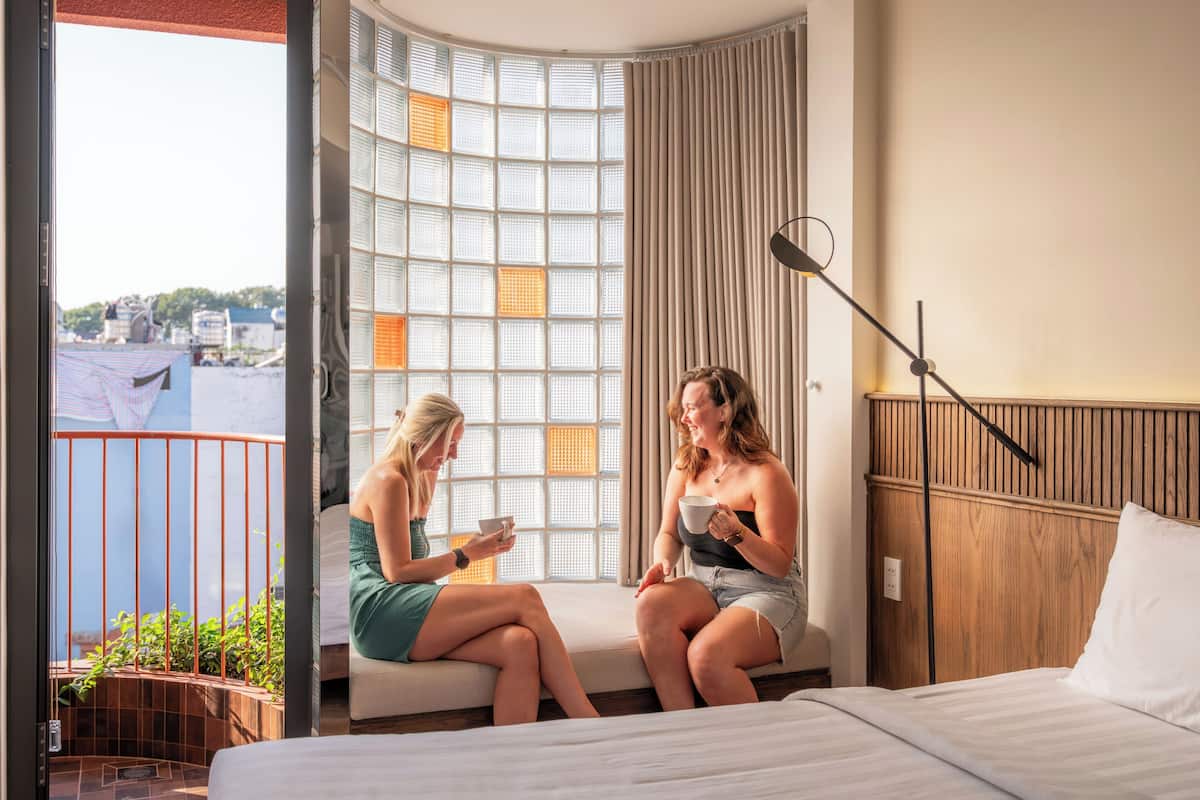 A hotel room with a bed, a window with a view, a balcony, and a seating area.