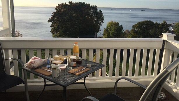 En balkong med ett bord dukat för frukost, med utsikt över en vattenyta där man i fjärran kan se fartyg.