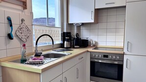 Ett kök med diskho, spis, skåp och ett fönster med utsikt över ett snötäckt landskap.