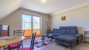 Uma sala de estar acolhedora com um sofá, uma mesa de jantar com cadeiras, um radiador e uma janela com vista para árvores.