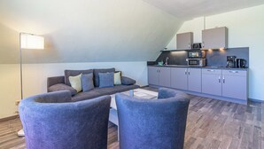 Un espacio habitable compacto con sofá, dos sillones, kitchenette e iluminación de techo.