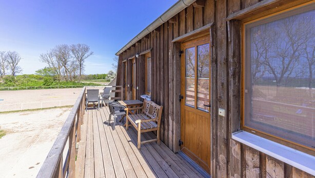 Una cabaña de madera con terraza, mobiliario exterior y ventanas amplias.