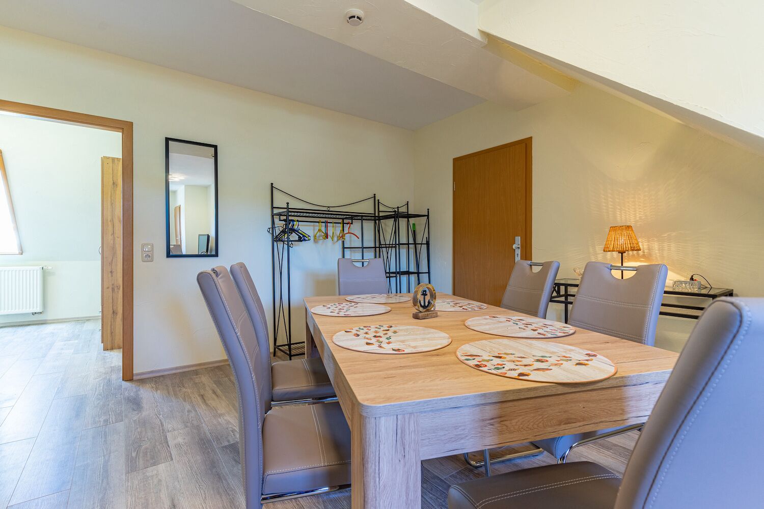 Un comedor con una mesa de madera, seis sillas, un perchero y una lámpara.