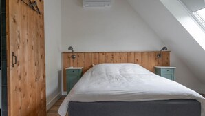 A bedroom with a sloped ceiling, a bed with a grey headboard, two bedside tables, and a wooden wardrobe.