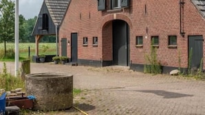 A brick building with a triangular roof, a flagpole with a flag, and a paved area with a stone structure.