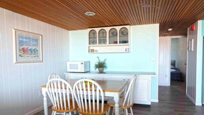 A kitchen with a wooden ceiling, white cabinetry, a microwave, and a dining table with chairs. - Cute, spacious 1-bedroom oceanfront condo with free WiFi, an outdoor pool, and an expansive balcony located midtown! (Ocean City)