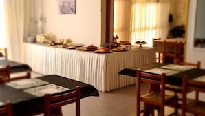 Un espace repas avec des tables et des chaises, un buffet garni de plats, et une porte qui donne sur une autre pièce.