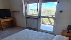 Une chambre à coucher avec un grand lit, un téléviseur posé sur un meuble en bois et une fenêtre donnant sur l’extérieur.