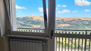 Une pièce dotée d’une grande fenêtre, d’un radiateur et offrant une vue sur un paysage vallonné.
