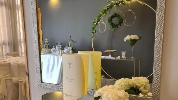 Un coin repas comprenant une table, des chaises, un vase avec des fleurs et un grand miroir au mur.