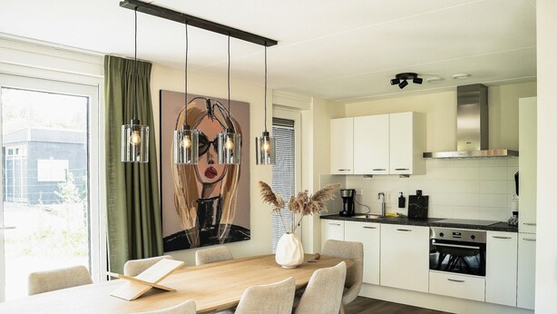 Una cucina moderna con mobili bianchi, un tavolo da pranzo in legno e lampade a sospensione.