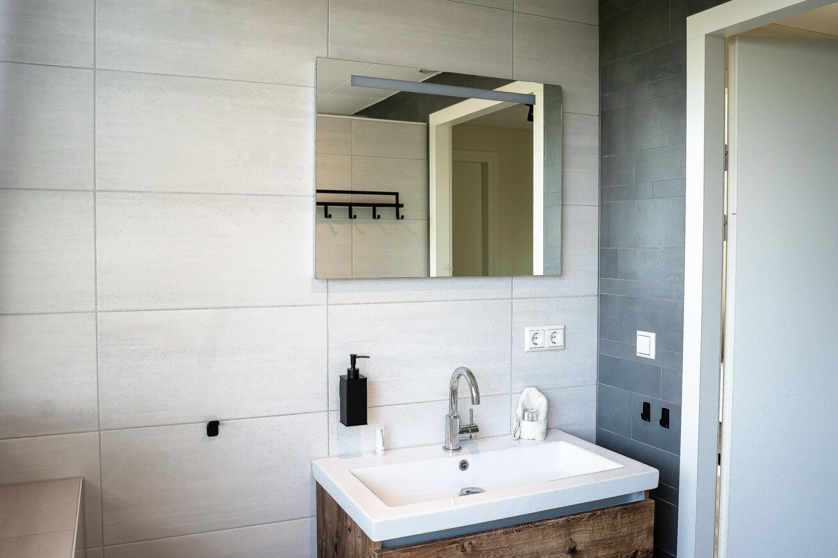 Un baño con un lavamanos blanco, un espejo y un dispensador de jabón negro.