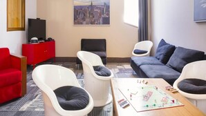 A hotel room with a cityscape painting, a red cabinet, a black sofa, white chairs, and a wooden coffee table with a board game. - Stylish Stay With Terrace & Wellness (Tignes)