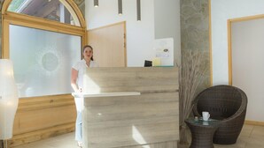 A reception area with a wooden reception desk, a large arched window, and a wicker chair. - Stylish Stay With Terrace & Wellness (Tignes)