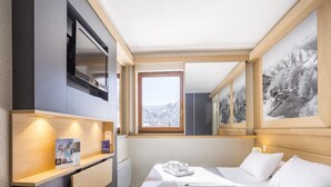 A hotel room with a bed, a desk, a TV, a window with a mountain view, and a framed picture on the wall. - Stylish Stay With Terrace & Wellness (Tignes)