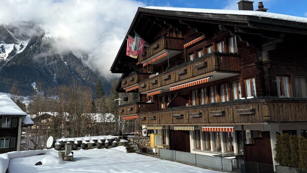 Un bâtiment en bois à plusieurs étages, doté de balcons, avec un sol enneigé et une chaîne de montagnes en arrière-plan.