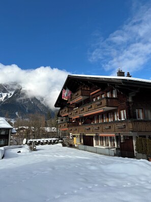 A multi-story wooden building with balconies, a snow-covered ground, and a mountain backdrop. - Apartment Thilo Very centrally located, small but nice, fully equipped apartment. (Lenk)