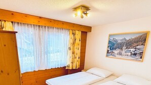 Une chambre avec deux lits, une armoire en bois, une chaise et une fenêtre avec des rideaux.