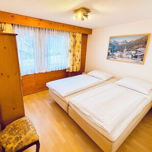 A room with two beds, a wooden wardrobe, a chair, and a window with curtains. - Apartment Thilo Very centrally located, small but nice, fully equipped apartment. (Lenk)