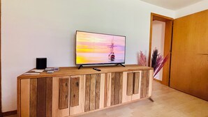 Un meuble en bois pour télévision, sur lequel est posée une télévision à écran plat affichant une scène de coucher de soleil, avec une télécommande et un haut-parleur sur le côté gauche.