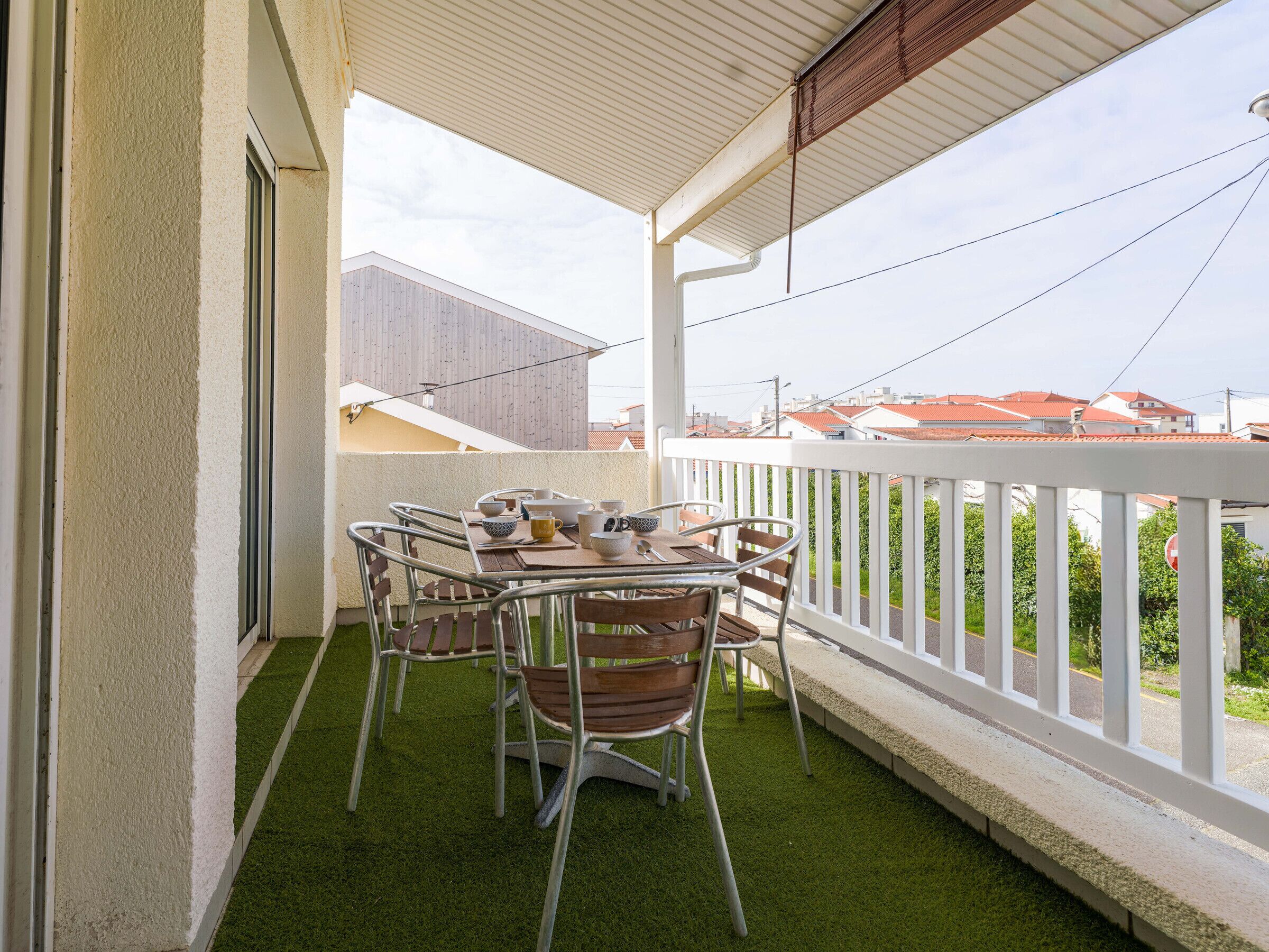 A balcony with a table and chairs, a view of the neighborhood, and a white railing.