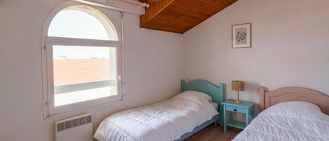 Ein Schlafzimmer mit zwei Betten, einem Fenster, einer Heizung und einer Decke mit Holzbalken.